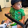 toddler, child, baby, stroller, cap, green_shirt, socks, toy, blanket, indoor, curious, seated, infant, grip, face, cheeks, clothing, footwear, person, casual