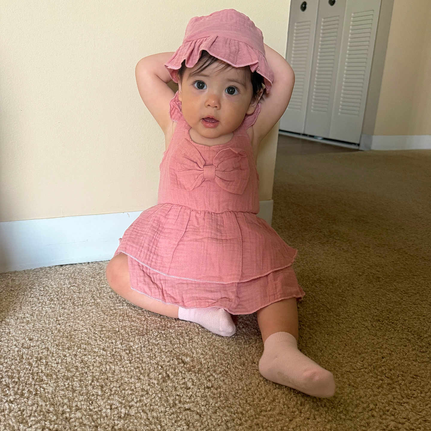 Hatyja joined the competition — help win amazing prizes! arms_up, carpet, child, clothing, curious, cute, door, expression, face, floor, home, indoor, person, pink_dress, pink_hat, sitting, sock, toddler, wall, young_child