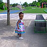 child, toddler, dress, playground, outdoor, sandy_ground, bench, tree, grass, greenery, park, shoes, person, daylight, playing, recreation, curious, young_child, nature, fun