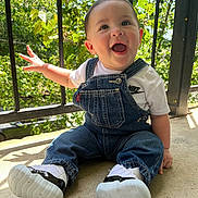 Eithan Loaiza is registered to the contest to win money with this photo: baby, child, smiling, denim_overalls, white_tshirt, nike_logo, sneakers, outdoor, sunlight, greenery, metal_railing, happy, cute, portrait, sitting, infant, casual_clothing, daylight, concrete_floor, expressive_face