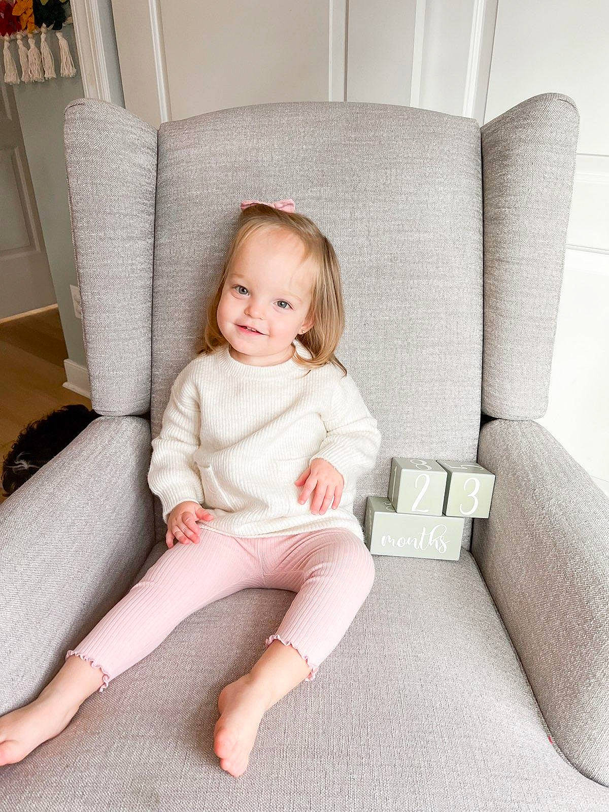 Kinsley is registered to the contest to win money with this photo: blond, child, comfort, couch, eye, floor, flooring, foot, furniture, human_body, human_leg, joy, knee, leg, living_room, person, product, room, sitting, smile