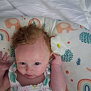 Feyre is registered to the contest to win money with this photo: baby, infant, flower, cushion, elephant_pattern, rainbow_pattern, curly_hair, blue_eyes, clothing, cute, child, portrait, indoor, soft_toy_pattern, smiling, head, hand, lying_down, fabric, colorful