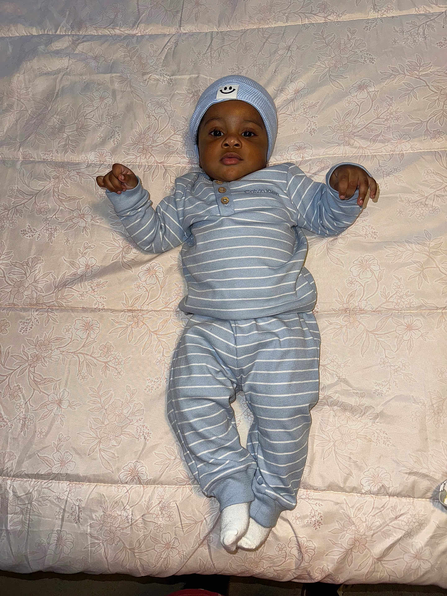 Kaden joined the competition — help win amazing prizes! baby, child, infant, bed, blanket, blue_clothing, striped_clothing, hat, sock, laying_down, face, person, indoors, cute, portrait, sleepwear, calm, young_child, smiling_face_patch, floral_pattern