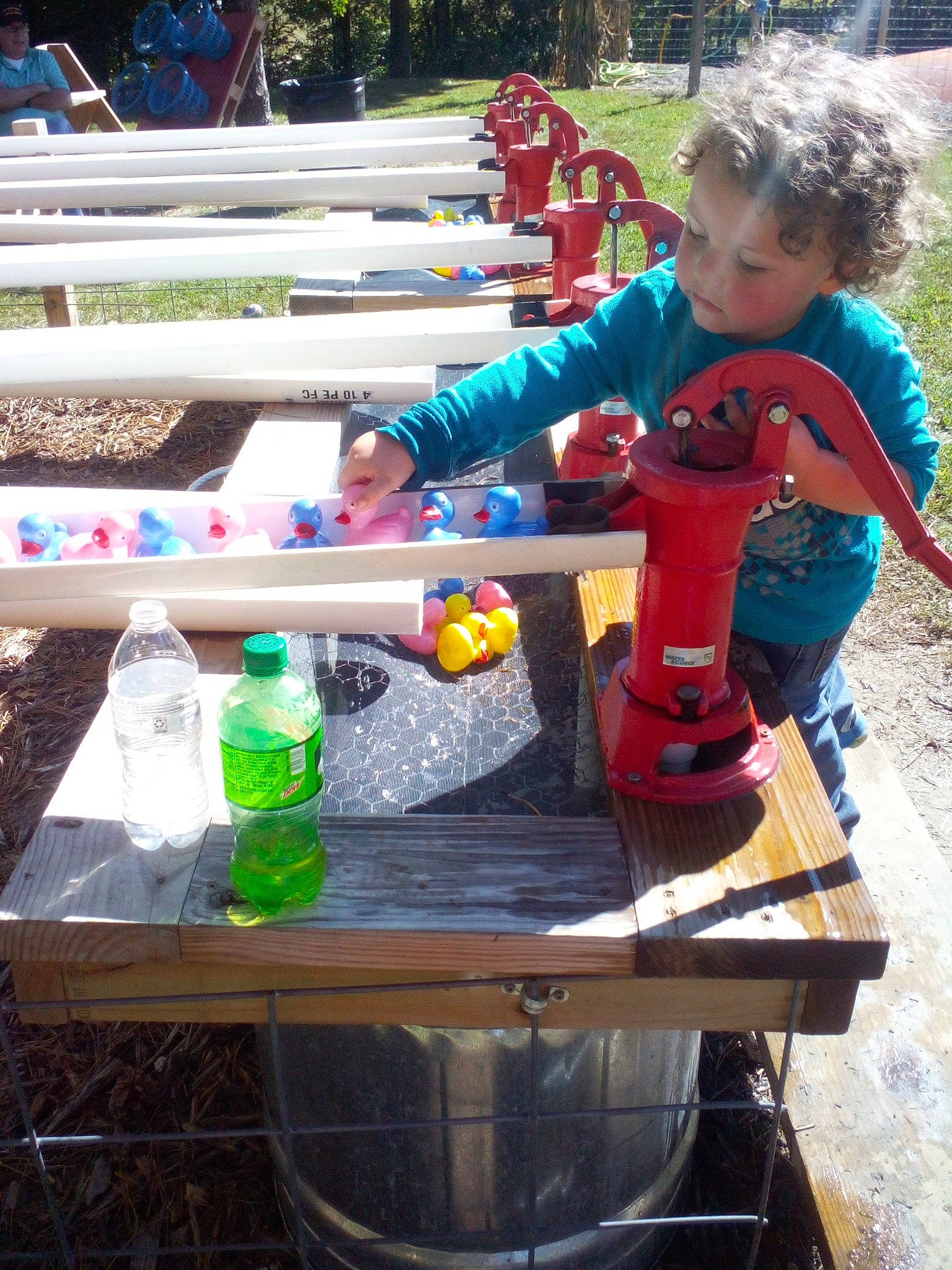 Ezekial is registered to the contest to win money with this photo: bottle, child, city, drink, drinking_water, fun, leisure, machine, person, plastic, plastic_bottle, play, recreation, sitting, soft_drink, soil, t_shirt, table, toddler, toy