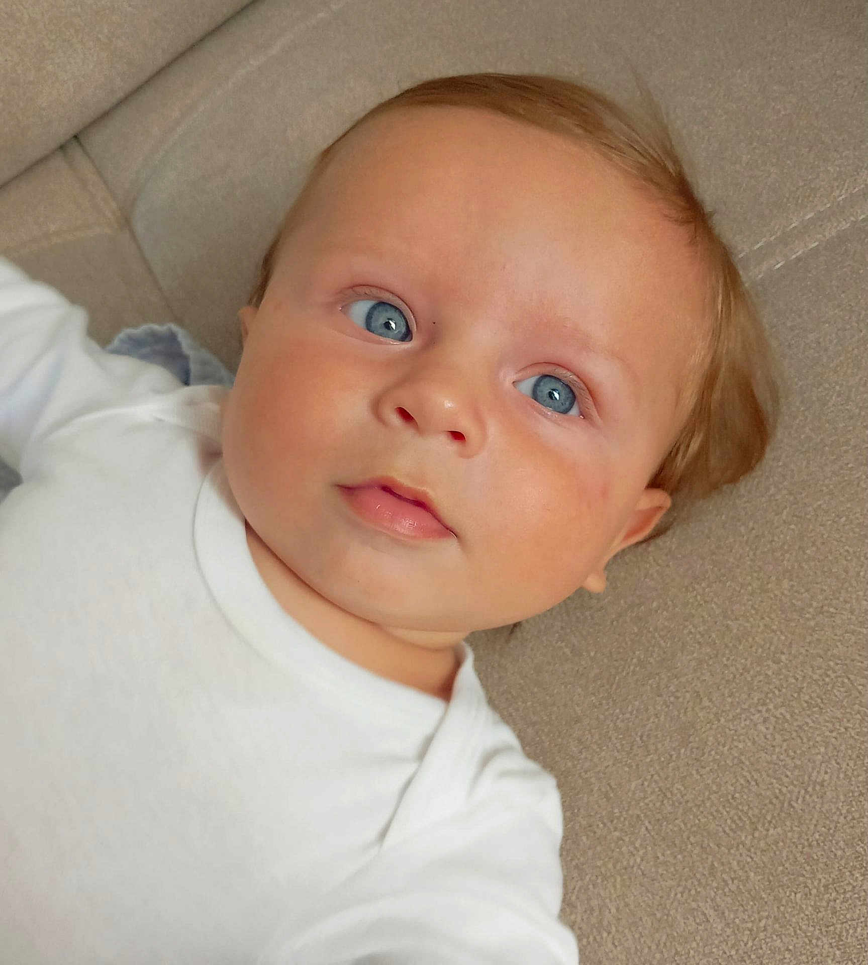Mahé a rejoint le concours — aidez-le/la à gagner de superbes lots ! baby, infant, face, blue_eyes, white_clothing, couch, cushion, soft_texture, closeup, child, person, portrait, cute, young, skin, head, expression, laying, indoors, peaceful