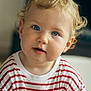 baby, blonde_hair, blue_eyes, casual_clothing, child, close_up, curious, curly_hair, cute, expression, face, indoors, innocent, person, portrait, red_and_white, soft_light, striped_shirt, toddler, young_child