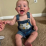 Cooper joined the competition — help win amazing prizes! baby, child, denim_overalls, teddy_bear, carpet, indoor, smiling, happy, hand_holding, person, cute, infant, sitting, skin, foot, face, young_child, joyful, casual_clothing, expression