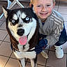 boy, child, dog, husky, blue_eyes, smiling, tongue_out, indoor, floor_tiles, white_chairs, clothing, gloves, jacket, sneakers, happy, pet, companion, cute, portrait, friendly