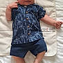 baby, infant, child, smiling, blue_shirt, shorts, palm_tree_pattern, blanket, lying_down, indoor, cute, happy, skin, foot, hand, face, clothing, button, fabric, bed