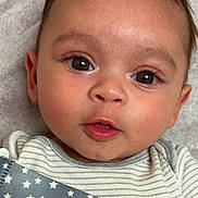 Yadiel is registered to the contest to win money with this photo: baby, infant, face, eyes, onesie, striped_clothing, star_pattern, strap, skin, head, cheeks, mouth, expression, lying_down, closeup, cute, young_child, portrait, person, indoors