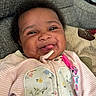 Amor is registered to the contest to win money with this photo: baby, smiling, tongue_out, child, infant, face, clothing, striped, floral, zipper, pink, couch, pillow, texture, happy, indoors, portrait, cute, person, young