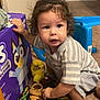 toddler, child, shoes, indoor, carpet, curly_hair, toy, box, blue_chair, clothing, sock, play, curious, brown_shoes, black_shoes, yellow_toy, striped_shirt, candid, person, floor