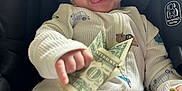 Walker is registered to the contest to win money with this photo: baby, child, car_seat, onesie, money, dollar_bill, smiling, tongue_out, playful, infant, clothing, seatbelt, car_safety, cute, happy, indoor, person, holding, small_hand, closeup