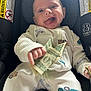baby, child, car_seat, onesie, money, dollar_bill, smiling, tongue_out, playful, infant, clothing, seatbelt, car_safety, cute, happy, indoor, person, holding, small_hand, closeup