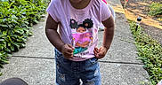Monaya is registered to the contest to win money with this photo: cars, casual_clothing, child, curly_hair, daytime, denim_shorts, greenery, happy, outdoor, person, pink_shirt, plants, play, shoes, sidewalk, smiling, suburban, sunlight, toddler, tricycle