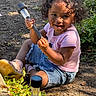 Monaya is registered to the contest to win money with this photo: child, curly_hair, cute, daylight, denim_shorts, dirt, garden_light, greenery, happy, nature, outdoor, person, pink_shirt, plants, playful, shoes, sitting, smile, sunlight, toddler