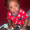 Kaden joined the competition — help win amazing prizes! toddler, child, baby, pajamas, stars, hair_buns, sandal, indoor, curious, patterned_surface, hand, footwear, person, cute, young_child, sitting, looking, bright_eyes, red_clothing, black_socks