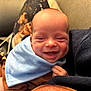 Greyson is registered to the contest to win money with this photo: baby, smiling, infant, blue_bib, brown_clothing, couch, pillow, dog_print, hand, face, happy, indoors, closeup, person, head, skin, child, sitting, cozy, soft