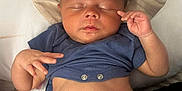 Reggie is registered to the contest to win money with this photo: baby, sleeping, hat, blue_shirt, diaper, hand, pillow, infant, peaceful, indoors, skin, face, closed_eyes, lying_down, newborn, cute, relaxed, child, human, tender