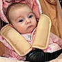baby, infant, pink_clothing, stroller, seat_belt, padded_straps, face, head, wide_eyes, curious, quilted_background, close_up, child, young, indoors, soft_lighting, portrait, baby_girl, warm_colors, cuteness