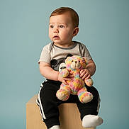Kameron joined the competition — help win amazing prizes! toddler, child, plush_toy, teddy_bear, sitting, wooden_block, soft_background, curious_expression, short_sleeves, casual_wear, black_pants, white_socks, studio_photo, indoor, cute, portrait, baby, toy, childhood, innocence