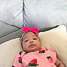 baby, infant, pink, headband, bow, strawberry_print, pillow, couch, gray, clothing, child, portrait, indoors, cute, lying_down, soft_furniture, young_child, person, casual, relaxed