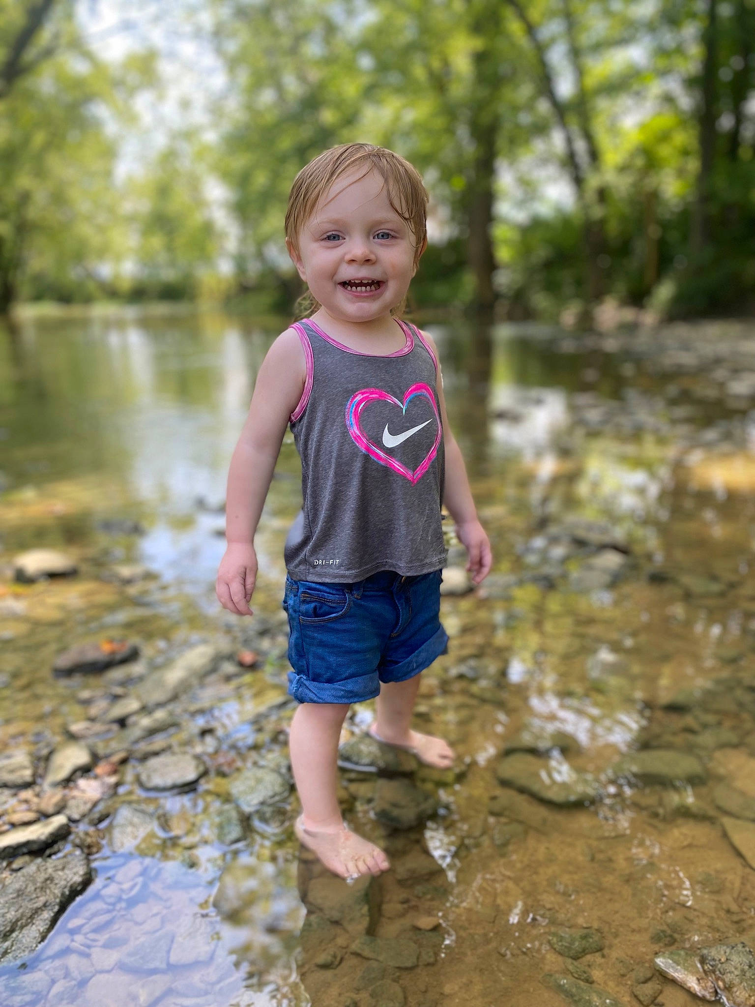 Kaleah is registered to the contest to win money with this photo: bank, forest, fun, grass, happy, joy, lake, leisure, natural_environment, people_in_nature, person, plant, recreation, shorts, smile, t_shirt, toddler, tree, water, water_resources