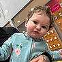 Hannah is registered to the contest to win money with this photo: toddler, child, person, fleece, zip_up, floral_pattern, curly_hair, blue_eyes, pouty_face, tattoo, hand, store_interior, accessories, display_board, indoor, casual_clothing, holding, cute, young_child, portrait
