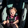 toddler, child, car_seat, seatbelt, curly_hair, blue_eyes, sunlight, vehicle_interior, sitting, pink_shirt, baby, young_child, safety_harness, car, portrait, cute, serious_expression, indoor, person, daylight