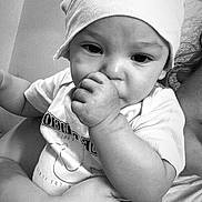 Ezra is registered to the contest to win money with this photo: baby, infant, child, hat, thumb_sucking, black_and_white, app_interface, social_media, screenshot, adult_arm, holding, cute, portrait, closeup, face, expression, text_overlay, mobile_screen, casual_clothing, headwear