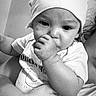 baby, infant, child, hat, thumb_sucking, black_and_white, app_interface, social_media, screenshot, adult_arm, holding, cute, portrait, closeup, face, expression, text_overlay, mobile_screen, casual_clothing, headwear