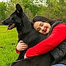 affection, black_dog, black_vest, casual_clothing, dog, grass, happy, hug, jeans, love, nature, outdoor, pet, portrait, red_sleeve, ripped_jeans, smile, tongue_out, trees, woman