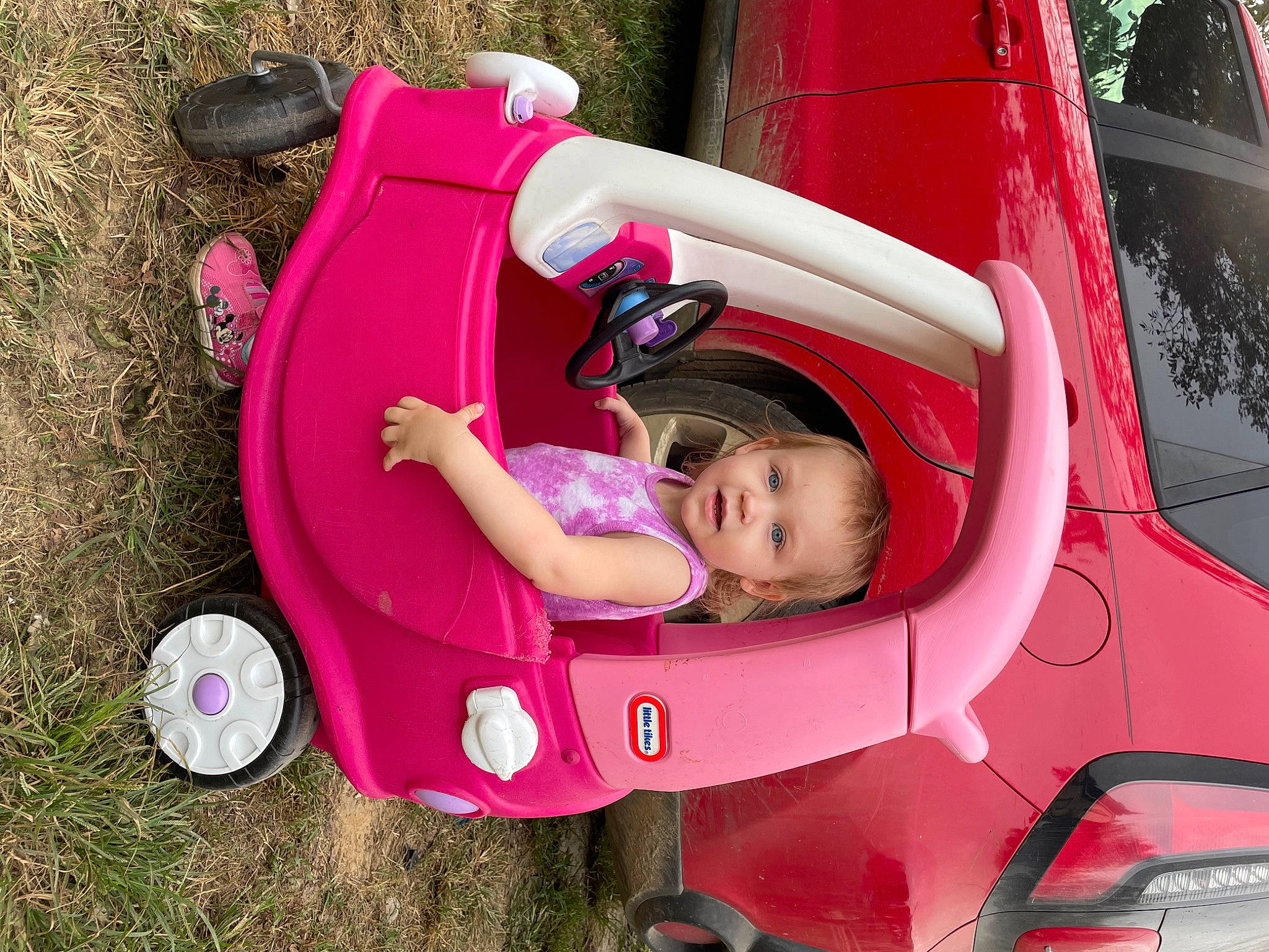 Athena is registered to the contest to win money with this photo: automotive_design, automotive_exterior, automotive_lighting, automotive_tire, bumper, car, fender, grass, hood, magenta, motor_vehicle, person, pink, plant, red, riding_toy, tire, vehicle, vehicle_door, wheel