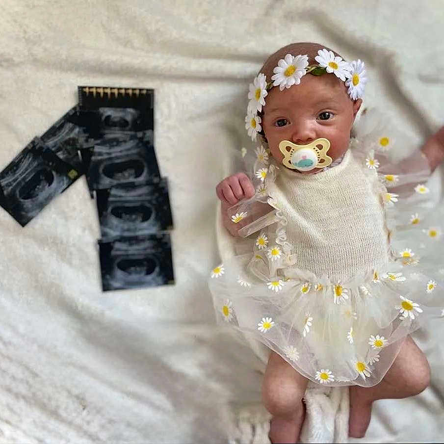 Ambre a rejoint le concours — aidez-le/la à gagner de superbes lots ! baby, blanket, child, clothing, cute, daisy, dress, flower, headband, human, infant, lying_down, newborn, pacifier, portrait, small, soft_texture, toddler, ultrasound, white