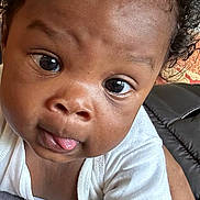Daylen is registered to the contest to win money with this photo: arm, baby, child, close_up, curly_hair, cute, expression, eyes, face, furniture, indoor, infant, pattern, person, pillow, portrait, skin, tongue, white_shirt, young