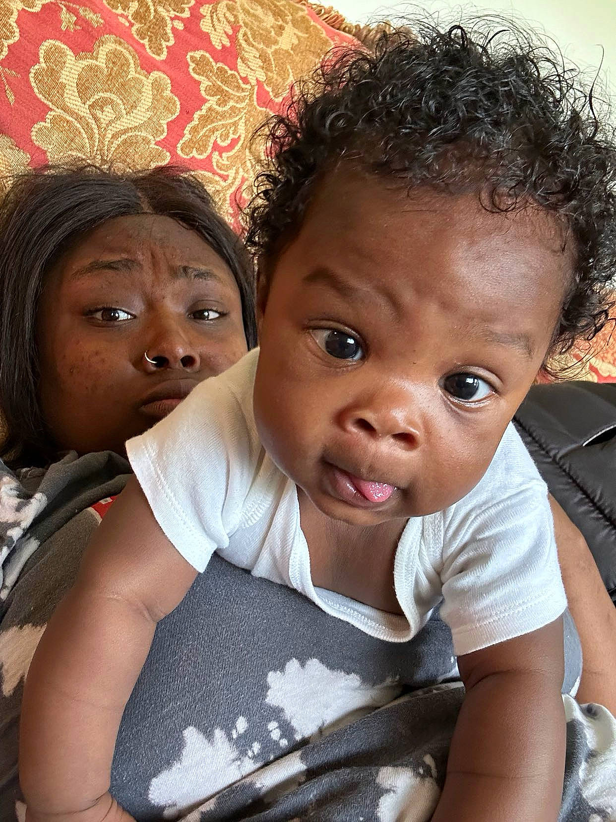 Daylen joined the competition — help win amazing prizes! adult, baby, child, close_up, couch, curly_hair, expression, face, gray_clothing, home, indoor, looking_at_camera, nose_ring, patterned_fabric, person, playful, portrait, resting, skin, white_shirt