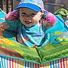 baby, child, cap, tie_dye, smile, baby_seat, colorful, outdoor, sunlight, grill, pattern, happy, playful, infant, cute, fabric, toy, seat, portrait, person
