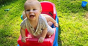 Roy is registered to the contest to win money with this photo: toddler, toy_wagon, grass, outdoor, sunlight, child, happy, smiling, play, summer, backyard, chair, truck, foot, plastic_toy, greenery, daylight, casual_clothing, recreation, nature
