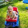 toddler, toy_wagon, grass, outdoor, sunlight, child, happy, smiling, play, summer, backyard, chair, truck, foot, plastic_toy, greenery, daylight, casual_clothing, recreation, nature