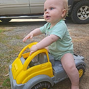 Roy joined the competition — help win amazing prizes! baby, child, toy_truck, outdoor, vehicle, green_clothing, curious, sitting, playtime, footwearless, gravel, daylight, side_view, cute, infant, small_toy, yellow, gray, parked_car, nature