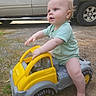 baby, child, toy_truck, outdoor, vehicle, green_clothing, curious, sitting, playtime, footwearless, gravel, daylight, side_view, cute, infant, small_toy, yellow, gray, parked_car, nature