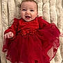 baby, smile, red_dress, heart_pattern, blanket, happy, infant, cute, tulle, fabric, child, portrait, lying_down, soft_texture, clothing, cheerful, baby_girl, toddler, warm, cozy