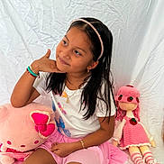 Yeimy is registered to the contest to win money with this photo: child, girl, portrait, sitting, smiling, indoors, bed, pink, doll, stuffed_animal, plush_toy, headband, long_hair, bracelets, necklace, skirt, toy, white_background, fashion, playroom