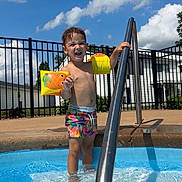 Kayson joined the competition — help win amazing prizes! child, pool, water, floaties, swim_trunks, metal_handrail, outdoor, summer, sunny, blue_sky, clouds, fence, building, happy, smiling, bare_chest, wet_hair, playing, recreation, daytime