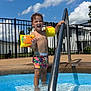 child, pool, water, floaties, swim_trunks, metal_handrail, outdoor, summer, sunny, blue_sky, clouds, fence, building, happy, smiling, bare_chest, wet_hair, playing, recreation, daytime