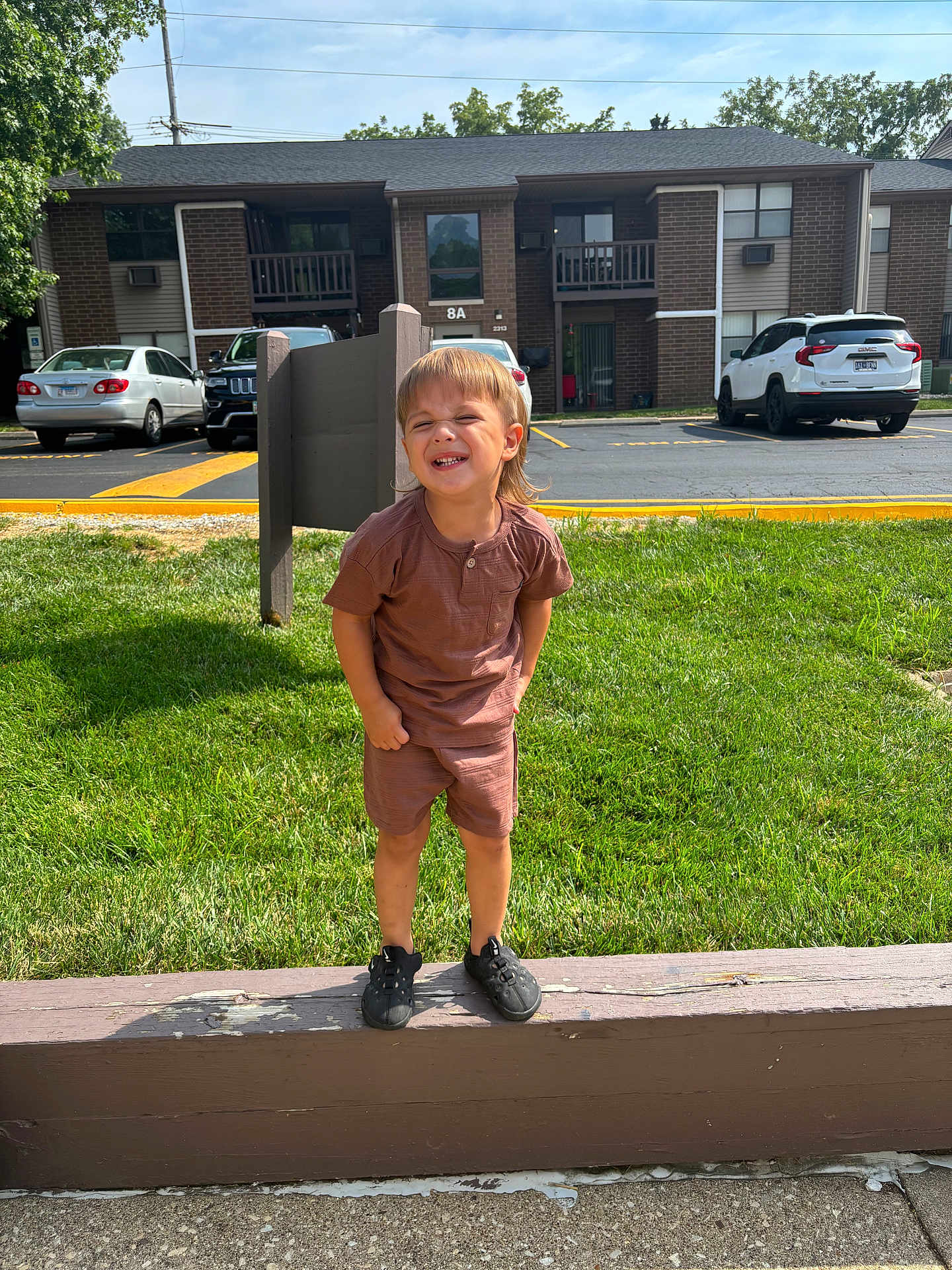 Kayson joined the competition — help win amazing prizes! child, boy, standing, smiling, outdoor, grass, building, apartment, car, parking_lot, concrete, wood, sunlight, casual_clothing, shorts, tshirt, black_shoes, happy, daytime, nature