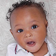 Keanu is registered to the contest to win money with this photo: baby, infant, face, curly_hair, white_shirt, close_up, cute, expression, child, portrait, skin, eyes, mouth, head, person, young_child, fluffy_background, indoor, adorable, curiosity
