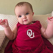 Hazel joined the competition — help win amazing prizes! baby, child, red_dress, cute, portrait, couch, quilted, indoor, smiling, hands, face, person, young_child, blue_eyes, skin, sleeveless, clothing, sitting, expression, infant