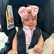 Neil is registered to the contest to win money with this photo: baby, infant, child, car_seat, pink_bow, headband, blanket, smile, cute, clothing, safety_harness, black, knitted, seat, indoor, portrait, person, happy, young, expression
