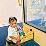 child, toddler, braids, white_shirt, blue_shoes, interactive_exhibit, wood, carpet, reflection, glass_panel, indoor, museum, play, seat, handle, curious, young, person, floor, casual_clothing